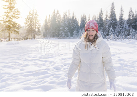 Joyful woman in winter coat enjoys snow play in snowy forest during bright sunny day Joyful woman in winter coat enjoys snow play in snowy forest during bright sunny day 130813308
