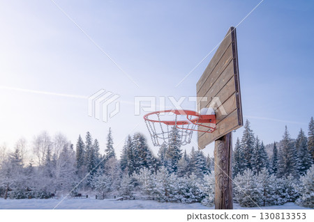 A basketball hoop in close-up on a snowy clearing in snow and frost against a beautiful coniferous forest. Playing basketball in winter. 130813353