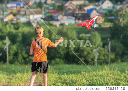 Boy enjoys summer by launching a radio-controlled airplane in an open area surrounded by nature 130813418