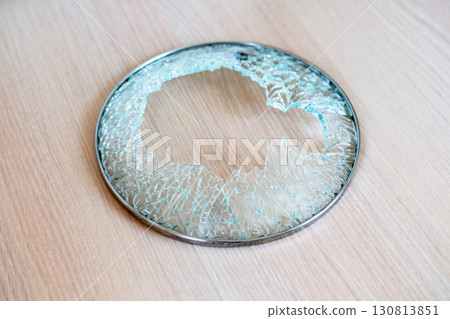 close-up shot of shattered glass circular lid with metal rim from cooking pot, resting on wooden surface, large central break with jagged, splintered edges, suddenness of an accident in kitchen close-up shot of shattered glass circular lid with metal rim from cooking pot, resting on wooden surface, large central break with jagged, splintered edges, suddenness of an accident in kitchen 130813851