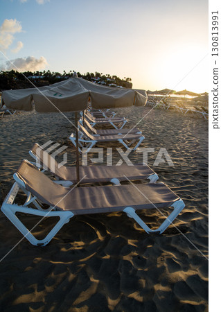 加那利群島富埃特文圖拉島上,沙灘床和遮陽傘排列在沐浴在清晨陽光下的沙灘海岸線上 加那利群島富埃特文圖拉島上,沙灘床和遮陽傘排列在沐浴在清晨陽光下的沙灘海岸線上 130813991