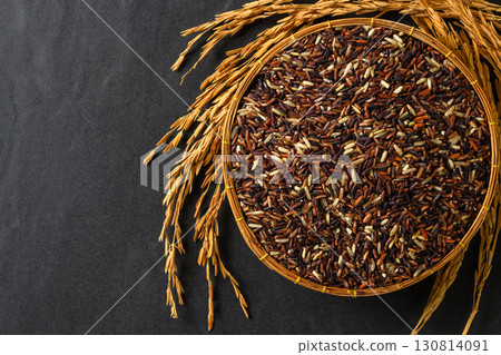 Top view of organic mixed rice grains in a bamboo basket with golden rice ears on black stone Background. Concept of healthy food, sustainable agriculture, and Asian cuisine ingredients. Top view of organic mixed rice grains in a bamboo basket with golden rice ears on black stone Background. Concept of healthy food, sustainable agriculture, and Asian cuisine ingredients. 130814091