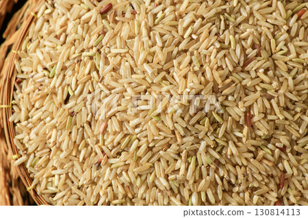 Top view of a round, traditional woven basket filled with uncooked brown rice grains. 130814113