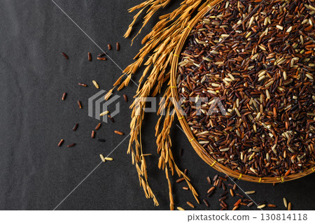 Top view of organic mixed rice grains in a bamboo basket with golden rice ears on black stone Background. Top view of organic mixed rice grains in a bamboo basket with golden rice ears on black stone Background. 130814118