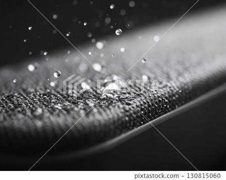Water droplets on a textured surface. Black and white macro shot showcasing liquid repellency, protection, and innovative material science. Ideal for tech, textile, and product concepts. 130815060