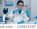 A dedicated female scientist in a white lab coat expertly uses a test tube and pipette, surrounded by lab equipment, meticulously exploring chemical reactions with precision and care 130815587