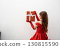 A graceful woman in a stunning red gown holds a beautifully wrapped gift against a minimalist background, embodying celebration and joyful anticipation for memorable moments ahead 130815590
