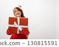 A cheerful young woman in a festive Santa hat and red dress holds a beautifully wrapped Christmas gift, embodying the warm spirit of the holiday season against a minimalist backdrop 130815591