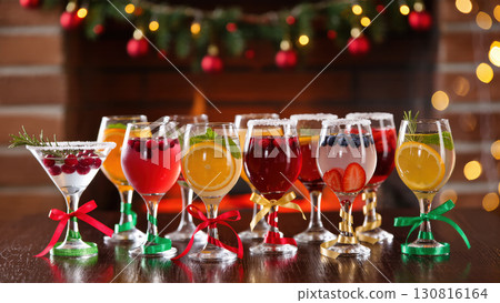 Christmas holiday cocktails with fruits and berries in decorated glasses on wooden table near fireplace and lights, festive party drinks 130816164