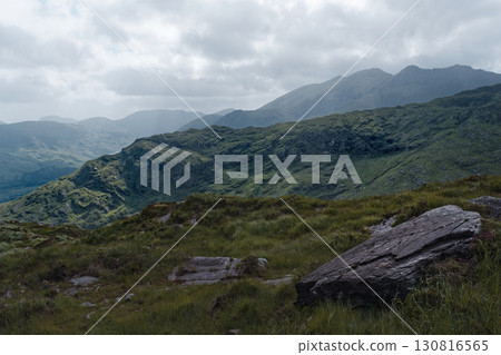Majestic mountains rise above a foreground of vibrant green grass and a large, weathered rock. A tranquil scene of untouched natural beauty. Majestic mountains rise above a foreground of vibrant green grass and a large, weathered rock. A tranquil scene of untouched natural beauty. 130816565