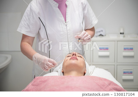 Beautician applying cosmetic treatment on female face with cotton swab in beauty salon 130817104