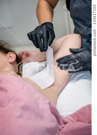 Beautician applying wax strip on female armpit during professional hair removal procedure 130817105