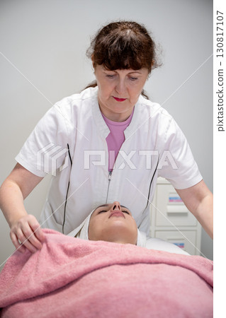 Beautician preparing female client for cosmetic facial treatment in professional beauty salon 130817107