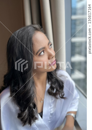 A young beautiful woman in a white silk robe in a hotel looks thoughtfully out the window 130817164