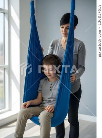 Autistic child boy wearing headphones in sensory swing therapy guided by therapist for calming sensory integration autism spectrum awareness and neurodiversity inclusion 130817615