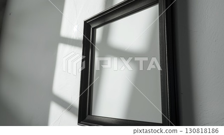 Ornate black picture frame with blank white background on textured wall, casting shadows in sunlight 130818186