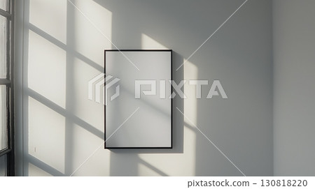 Black frame with a blank white canvas on a white wall in bright natural light and window shadow play 130818220