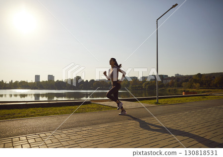 Female athlete running along city waterfront during outdoor workout on sunny summer day 130818531