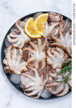 Fresh baby octopuses on ice, garnished with lemon and rosemary, on a marble table, no people, 130818726