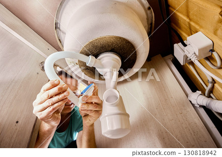 Sink trap with dishwasher machine inlet under basin in process of installation, plumber attaches overflow to corrugated hose. Sink trap with dishwasher machine inlet under basin in process of installation, plumber attaches overflow to corrugated hose. 130818942