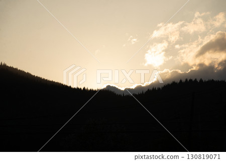 Golden sunlight peeks over mountain peaks at dusk, illuminating clouds and silhouetting trees in the valley Golden sunlight peeks over mountain peaks at dusk, illuminating clouds and silhouetting trees in the valley 130819071
