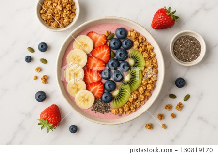 Bowl of colorful smoothie topped with fresh fruits, granola, and seeds on a marble background in a bright kitchen setting 130819170