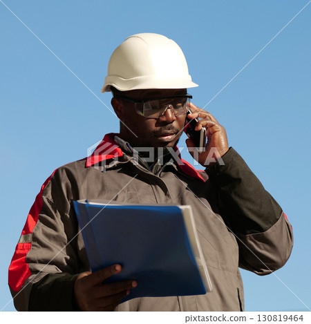 African american builder with work papers talks on smartphone 130819464