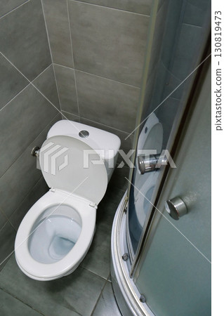 Toilet room interior with white toilet bowl, shower cabin, grey wall tiles 130819473