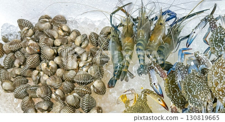 Array of fresh seafood, with glistening live crabs, prawns and a pile of shellfish on ice cubes, evokes the vibrant essence of ocean bounty. Perfect for culinary enthusiasts and seafood market 130819665