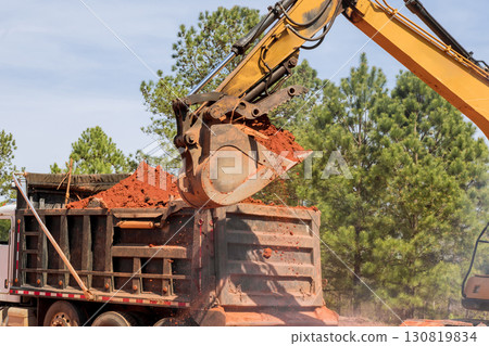 Construction equipment transfers soil into dump truck under works day near construction area. 130819834