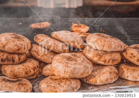 Freshly baked flatbreads stacked in piles on a grill, golden brown and rustic with smoky char marks. Concept of flatbread preparation and traditional street food flavor 130819913
