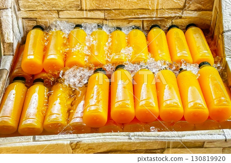 Rows of fresh orange juice in transparent bottles are chilled in water-filled, makeshift street cooler, showcasing a refreshing, healthy, summer beverage in vibrant street market setting 130819920