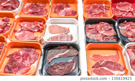 Array of fresh, raw fresh meat cuts neatly displayed in orange trays, offering a variety of choices for consumers seeking quality ingredients for home cooking Array of fresh, raw fresh meat cuts neatly displayed in orange trays, offering a variety of choices for consumers seeking quality ingredients for home cooking 130819925