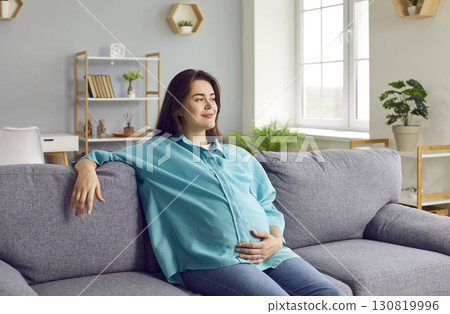 Happy beautiful pregnant woman relaxing on the couch and holding her hand on her belly 130819996