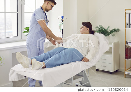 Fat woman lying on the couch in clinic while receiving IV drip infusion and vitamin therapy. Fat woman lying on the couch in clinic while receiving IV drip infusion and vitamin therapy. 130820014