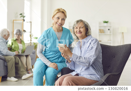 Happy Caregiver Helping Elderly Patient With Online Technology At Nursing Home 130820016