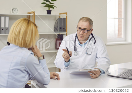 Middle aged doctor therapist consulting patient in medical office 130820032
