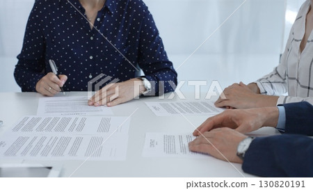 Business woman signing contract during a meeting with partners in contemporary office Business woman signing contract during a meeting with partners in contemporary office 130820191