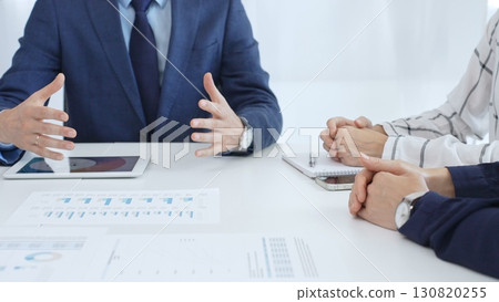 Business professionals discussing financial charts on tablet, collaborating closely while reviewing project data in modern corporate workspace 130820255