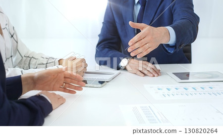 Business partners shaking hands at a meeting, celebrating successful negotiations and signing a contract, with documents, digital tablet, and smartphone on the table Business partners shaking hands at a meeting, celebrating successful negotiations and signing a contract, with documents, digital tablet, and smartphone on the table 130820264