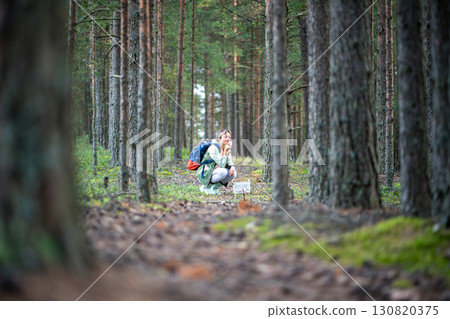 Woman smelling freshly picked mushroom on forest clearing surrounded by pine trees and pathway 130820375