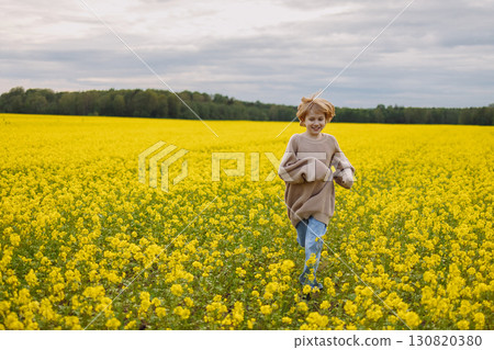 Smiling 9 year old girl in oversize sweater running in yellow rapeseed field 130820380