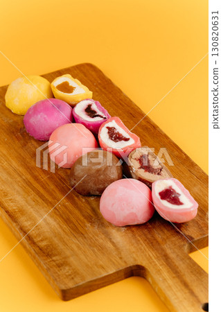 Assorted mochi ice cream on wooden board over vibrant yellow background, flat lay 130820631