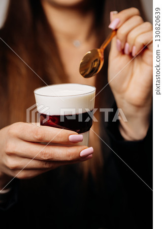 Woman holding creamy dessert with cherry jelly in glass and golden spoon 130820639
