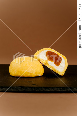 Yellow mochi ice cream with creamy filling and apricot jam on a dark stone plate 130820643