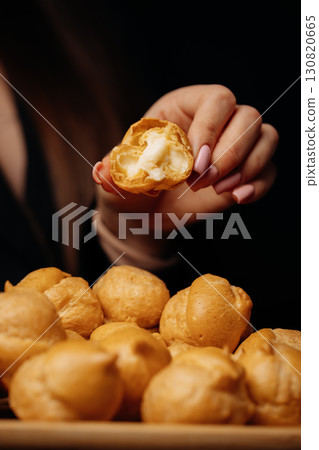 Woman holding a bitten cream puff over a tray of profiteroles in elegant setting 130820665