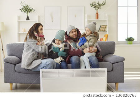 Unhappy parents, small children freezing at home wearing winter warm clothes near radiator Unhappy parents, small children freezing at home wearing winter warm clothes near radiator 130820763