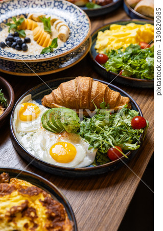 Healthy breakfast with croissant, avocado, sunny side eggs and salad on dark background Healthy breakfast with croissant, avocado, sunny side eggs and salad on dark background 130820985