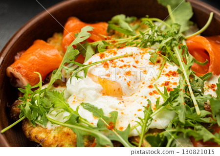 Healthy brunch with poached egg, smoked salmon and fresh arugula on a vegetable fritter Healthy brunch with poached egg, smoked salmon and fresh arugula on a vegetable fritter 130821015