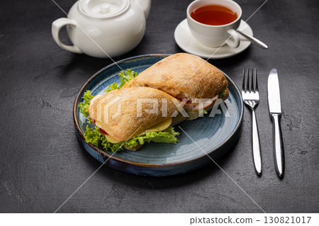 Ciabatta sandwich with cheese, ham and lettuce served with tea on a rustic black background Ciabatta sandwich with cheese, ham and lettuce served with tea on a rustic black background 130821017